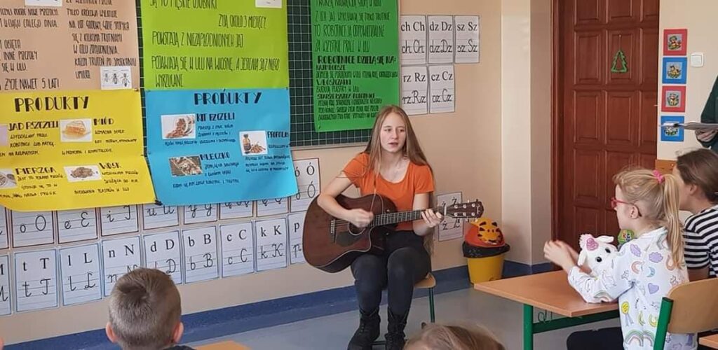licealistka grająca na gitarze dla uczniów podstawówki w klasie